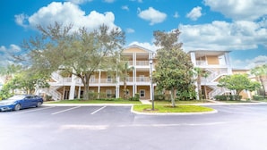 A multi-story hotel with a central courtyard, a parking lot, and a blue car parked in front. - It1072 - 3 Condo in Bahama Bay Resort, Sleeps Up To 6, Just 5 Miles To Disney (Davenport)