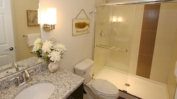 A bathroom with a granite countertop, a sink, a toilet, and a glass-enclosed shower.