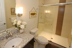 A bathroom with a granite countertop, a sink, a toilet, and a glass-enclosed shower.