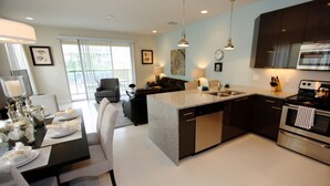 A modern kitchen with dark cabinetry, a central island, and a dining area with a table set for four. - It2561 - 3 Townhome in Serenity, Sleeps Up To 7, Just 5 Miles To Disney (Clermont)
