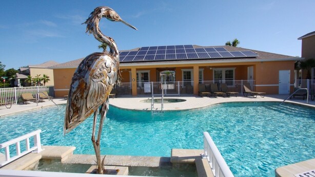 A pool area with a bird sculpture, a solar panel roof, and a building with a balcony. - It2561 - 3 Townhome in Serenity, Sleeps Up To 7, Just 5 Miles To Disney (Clermont)