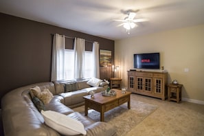 A living room with a sectional sofa, a wooden coffee table, a TV on a wooden cabinet, and a ceiling fan.
