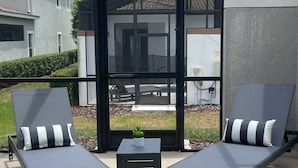 A modern outdoor seating area with two lounge chairs and a small table, enclosed by a glass door and a black frame. - It2852 - 5 Townhome in Storey Lake Resort, Sleeps Up To 10, Just 9 Miles To Disney (Kissimmee)