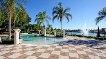 A pool area with a checkered floor, palm trees, and a fountain in the background.