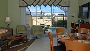 A living room with a pool view, including a sofa, chairs, a dining table, and a TV. - Grh9369ha - Windsor Hills Resort - 3 Bed 3 Baths Townhome (Kissimmee)