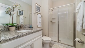 A bathroom with a granite countertop, a potted plant, a toilet, a shower with a glass door, and framed artwork on the wall. - Grh9379ha - Champions Gate Resort - 4 Bed 3 Baths Townhome (Davenport)