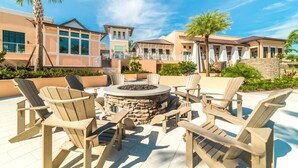 An outdoor seating area with Adirondack chairs and a stone fire pit, surrounded by a landscaped garden and a building with a balcony. - Grh9389ha - Solara Resort - 4 Bed 3 Baths Villa (Kissimmee)