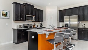 A modern kitchen with dark cabinetry, stainless steel appliances, a granite countertop, and a central island with bar stools. - Grh9389ha - Solara Resort - 4 Bed 3 Baths Villa (Kissimmee)