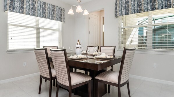 A dining room with a dark wooden table, six upholstered chairs, and a chandelier. - Grh9402ha - Solara Resort - 4 Bed 3.5 Baths Villa (Kissimmee)