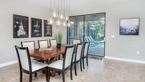 A dining area with a wooden table, six chairs, and hanging pendant lights. There are three framed pictures on the wall. - Grh9451ha - Champions Gate Resort - 5 Bed 4.5 Baths Villa (Davenport)