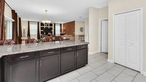 A modern kitchen with dark cabinets, a granite countertop, and a dining area with brown leather chairs. - Fs9493ha - Champions Gate Resort - 6 Bed 6 Baths Villa (Davenport)