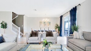 A modern living room with a glass coffee table, two sofas, a chandelier, and a staircase. - Fs9526ha - Champions Gate Resort - 8 Bed 5 Baths Villa (Davenport)
