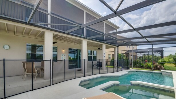 A covered outdoor swimming pool area with lounge chairs and a patio table, surrounded by a fence. - Fs9534ha - The Shire at West Haven - 5 Bed 4 Baths Villa (Davenport)