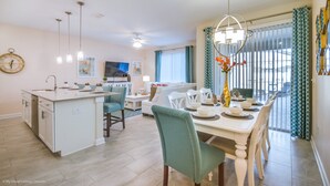 A modern kitchen with a central island, dining area with a white table and chairs, and a living room with a sofa and TV. - Fs9554ha - Storey Lake Resort - 4 Bed 3 Baths Townhouse (Kissimmee)