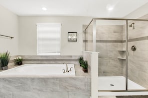 Une salle de bain avec une baignoire, une douche et une fenêtre équipée de stores.