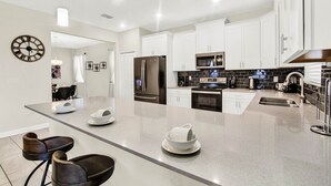 Una cocina moderna con armarios blancos, una isla grande, electrodomésticos de acero inoxidable y un reloj en la pared.