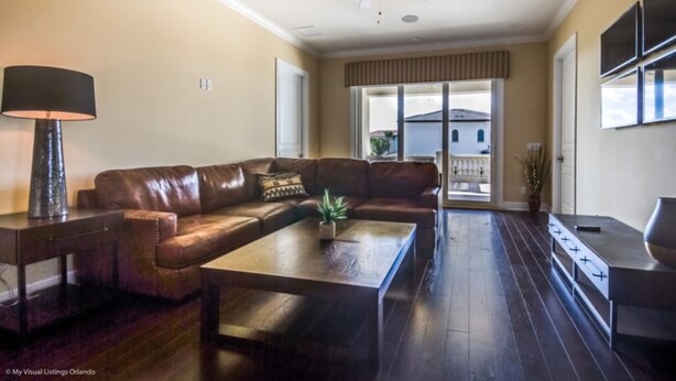 Una sala de estar con un sofá de cuero marrón, una mesa de centro de madera, un ventilador de techo y un televisor en la pared.
