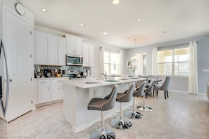 A modern kitchen with white cabinets, a central island with bar stools, a microwave, and a sink. - Fs9605ha - Solara Resort - 4 Bed 3.5 Baths Villa (Kissimmee)