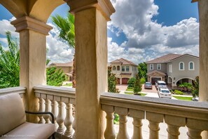 Zona residencial com varanda, colunas e vista para casas sob um céu claro.