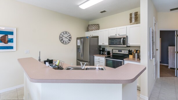 A modern kitchen with white cabinetry, a central island, stainless steel appliances, and a wall clock. - Fs9629ha - Bella Vida Resort - 4 Bed 3 Baths Townhouse (Kissimmee)