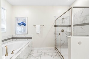 Ein modernes Badezimmer mit einer gläsernen Duschkabine, einer großzügigen Badewanne und einem Boden aus Marmorfliesen.
