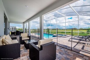 A covered outdoor area with wicker furniture, a pool, and a view of the landscape. - Fs9634ha - Champions Gate Resort - 9 Bed 5 Baths Villa (Davenport)