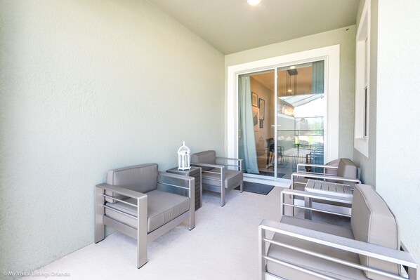 A balcony with outdoor seating, a glass door leading to a patio, and a small white lantern on a table.