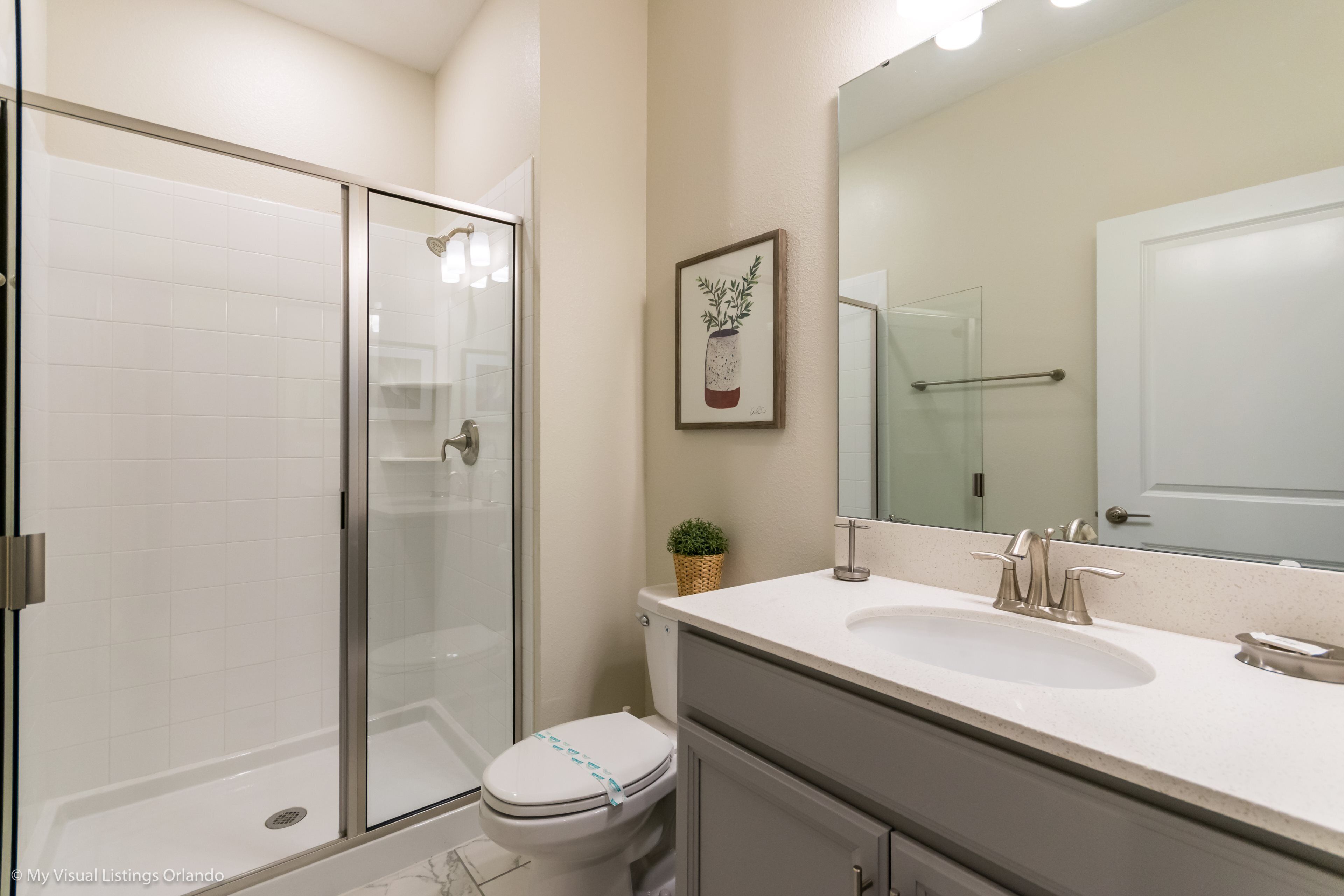 A bathroom with a glass shower enclosure, a toilet, a sink, and a mirror.