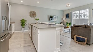 A modern kitchen with white cabinetry, a central island, and a dining area with a sofa and a TV.