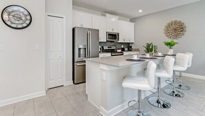 A modern kitchen with white cabinetry, stainless steel appliances, a central island with bar stools, and decorative wall art.