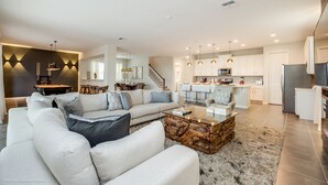 Ein modernes Wohnzimmer mit einer Eckcouch, einem Couchtisch und einer Küchenzeile mit weißen Schränken und Edelstahlgeräten.