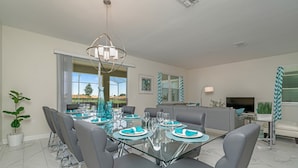 A modern dining area with a glass table, grey chairs, and teal accents. - Fs9717ha - Champions Gate Resort - 9 Bed 5 Baths Villa (Davenport)