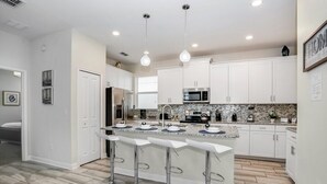 A modern kitchen with white cabinets, a granite countertop, and a central island with bar stools. - Fs9741ha - Storey Lake Resort - 5 Bed 5 Baths Villa (Kissimmee)
