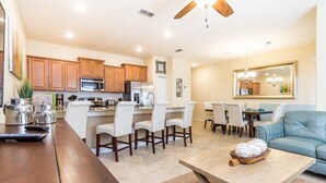 A modern kitchen with wooden cabinets, a dining area with white chairs, and a living room with a blue sofa and a coffee table. - Fs9776ha - Storey Lake Resort - 4 Bed 3 Baths Townhouse (Kissimmee)