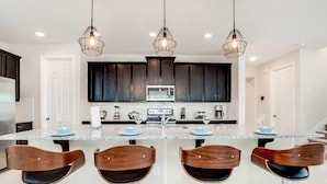 Una cocina moderna con armarios oscuros, una isla central con taburetes altos e iluminación colgante.