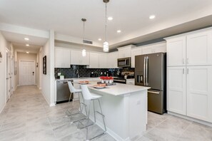 A modern kitchen with white cabinets, stainless steel appliances, and a central island with bar stools. - Fs9791ha - Storey Lake Resort - 2 Bed 2 Baths Condo (Kissimmee)