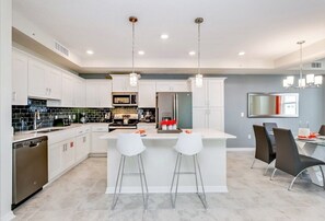 A modern kitchen with white cabinets, a central island with bar stools, and a dining area with a gray wall and a large mirror. - Fs9791ha - Storey Lake Resort - 2 Bed 2 Baths Condo (Kissimmee)