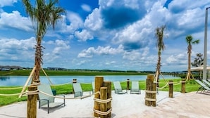 Un espace extérieur paisible avec un lac, des chaises longues et des palmiers.