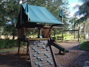A wooden playground structure with a slide and climbing net, surrounded by trees and a clear sky. - Fs9810ha - Glenbrook Resort - 4 Bed 3.5 Baths Villa (Clermont)