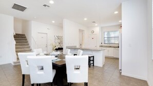 A modern kitchen with white cabinets, a central island, and a dining area with white chairs. - Fs9823ha - Providence - 4 Bed 4 Baths Villa (Davenport)