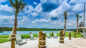 A serene outdoor area with a lake, lounge chairs, and palm trees. - Fs9826ha - Storey Lake Resort - 9 Bed 5 Baths Villa (Kissimmee)