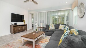 A modern living room with a sectional sofa, a wooden coffee table, a flat-screen TV, and a decorative wall piece. - Grh9164ha - Solara Resort - 7 Bed 6.5 Baths Villa (Kissimmee)