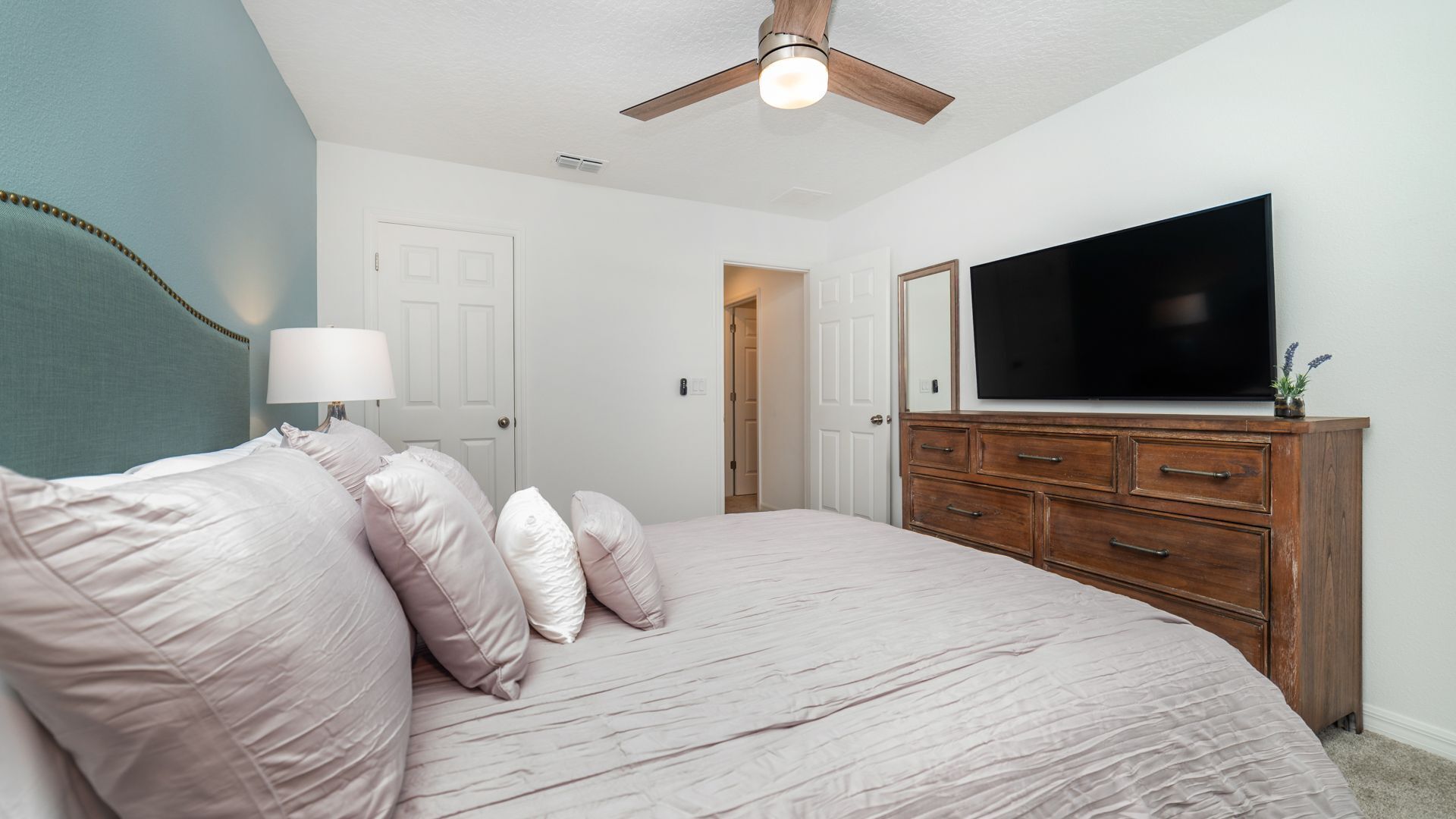 A bedroom with a bed, a dresser, a television, and a ceiling fan.