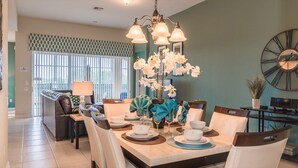 A dining area with a table set for four, surrounded by chairs. There is a chandelier above the table, and a large clock on the wall. - Grh9174ha - Windsor Hills Resort - 4 Bed 4 Baths Villa (Kissimmee)
