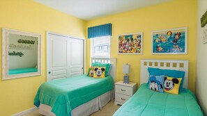 A room with two beds, each with green bedding and Mickey Mouse pillows, a white door, and two framed pictures on the wall. - Grh9174ha - Windsor Hills Resort - 4 Bed 4 Baths Villa (Kissimmee)