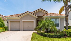 A two-story house with a tiled roof, two garage doors, and a well-maintained lawn with a palm tree. - Grh9174ha - Windsor Hills Resort - 4 Bed 4 Baths Villa (Kissimmee)
