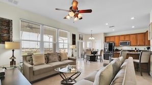 A spacious living room with a sofa, coffee table, and dining area. There is a kitchen with wooden cabinets and a refrigerator. - Grh9175ha - Windsor Hills Resort - 6 Bed 5 Baths Villa (Kissimmee)