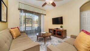 A living room with a sofa, a coffee table, a TV, and a sliding glass door. - Grh9185ha - Windsor Hills Resort - 3 Bed 2 Baths Condo (Kissimmee)