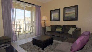 A living room with a sofa, armchair, ottoman, and a balcony with a table and chairs. - Grh9192ha - Windsor Hills Resort - 3 Bed 2 Baths Condo (Kissimmee)