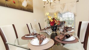 Une table à manger est dressée pour quatre personnes, avec des sets de table, des assiettes, des couverts et des verres à vin. Un vase rempli de fleurs est placé au centre de la table.
